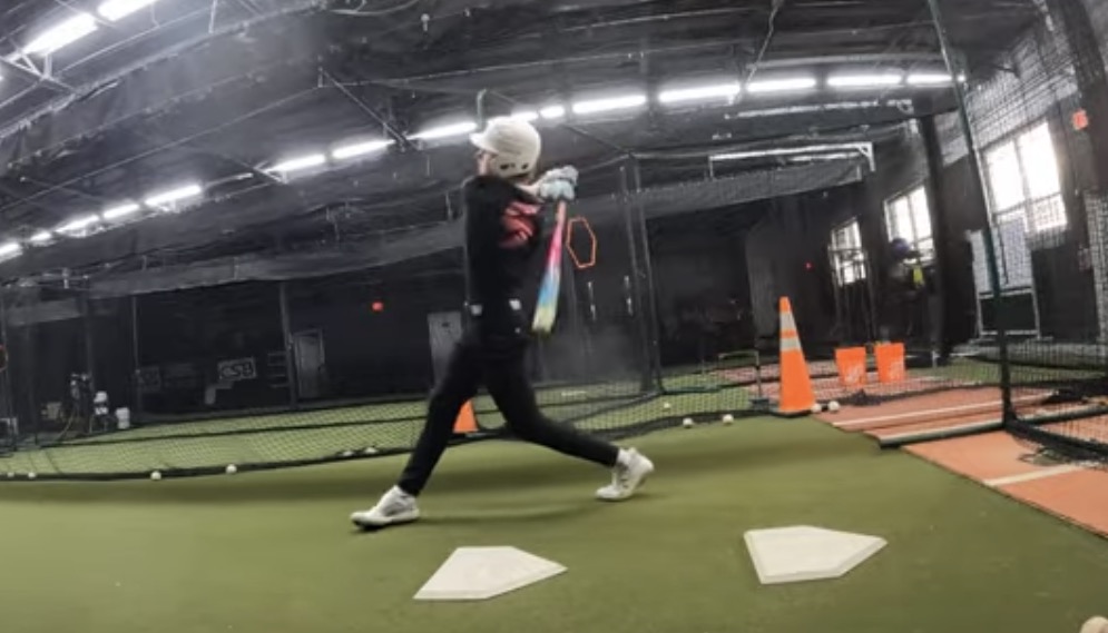 Young hitter completing a swing during an indoor baseball training session