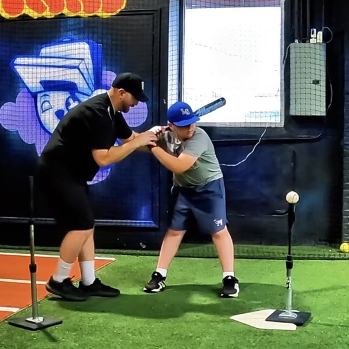 Coach Steve guiding a young hitter's hands and bat path at the tee