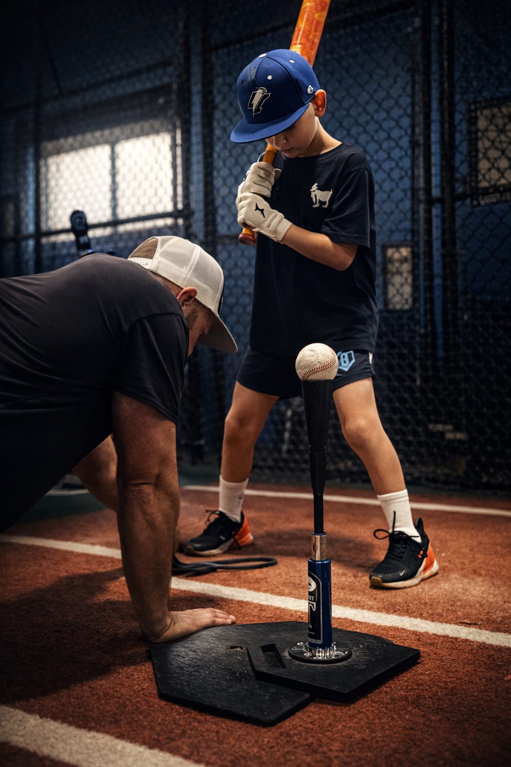 Coach Steve kneeling at the plate while a young hitter in a blue cap sets up for tee work